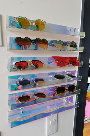 Shelves holding five rows of sunglasses, mounted on the reviewer's wall.
