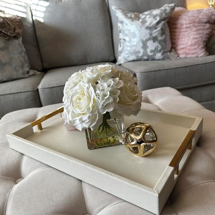 A reviewer's decorative tray holding a vase of white flowers and a gold ornament, placed in front of a sofa.