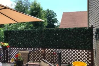 A reviewer's photo showing faux ivy placed on the top section of a fence, providing privacy in a backyard