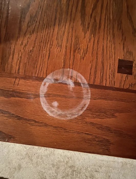 A visible white watermark ring on a reviewer's wooden table, clearly showing the damage