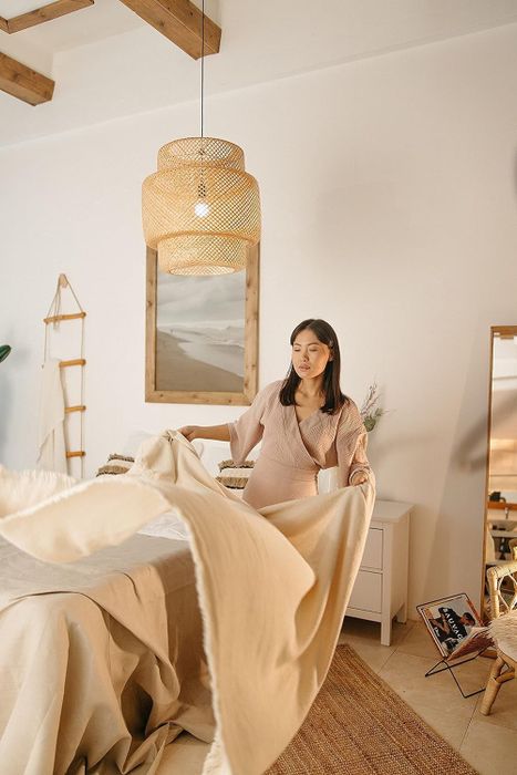 A three-tier woven pendant light made from rattan, with a person seen making their bed beneath the light.