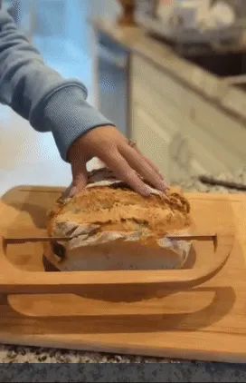 A person using a bow cutter knife to slice freshly baked bread.