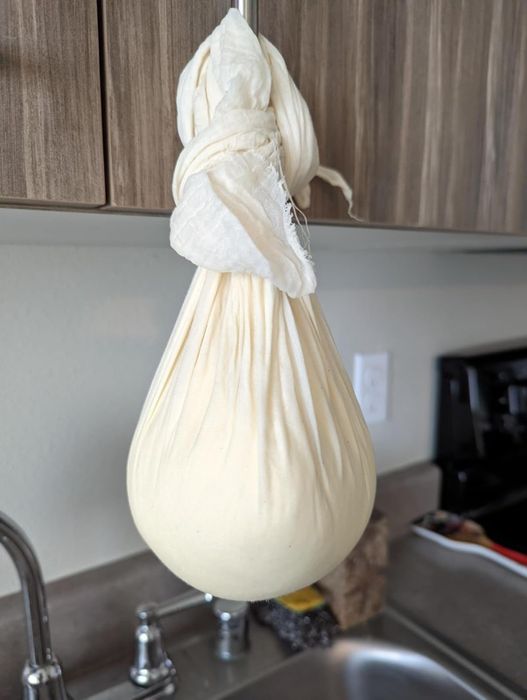 A bundle of cheesecloth hanging over a kitchen sink, likely being used to strain homemade cheese or yogurt