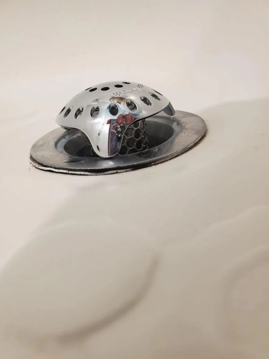 A close-up of a shower drain cover with a dome shape and multiple small holes designed to catch hair