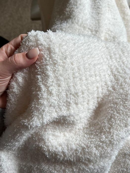 A reviewer wrapped up in a luxuriously soft white plush blanket, radiating pure comfort.