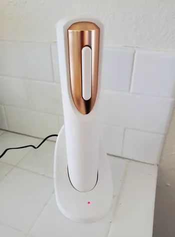 A cordless automatic wine opener with a charging base sitting on a white countertop.