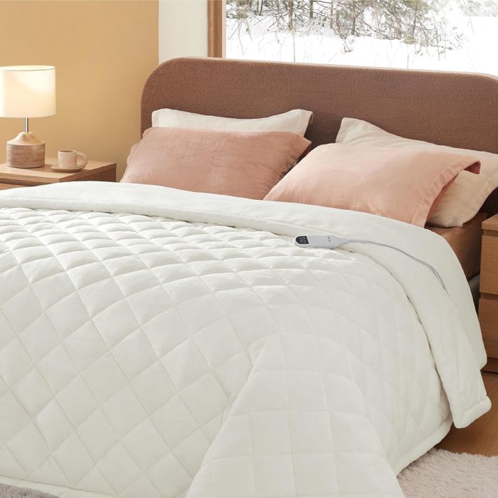 A cozy bedroom with a quilted blanket on the bed, two pillows, and a bedside lamp, all coming together to create a warm and inviting space
