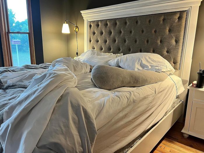 A bed with an unmade duvet, featuring a headboard and pillows, placed in a cozy room with a nightstand and lamp