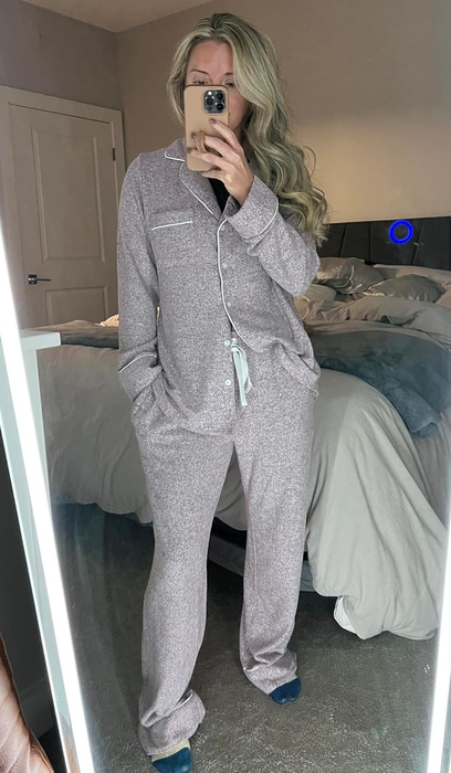 A person, clad in cozy pajamas, snaps a mirror selfie in their bedroom.