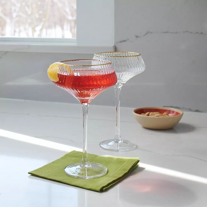 A set of elegant wine glasses filled with drinks, one garnished with a slice of lemon. The glasses are placed on a green napkin beside a bowl of nuts on a sleek marble countertop
