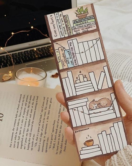 A person holding the bookmark with blank books arranged on painted shelves.