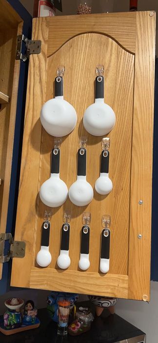 Measuring cups in various sizes, neatly arranged on a wooden cupboard door, hanging from hooks for easy access and storage.