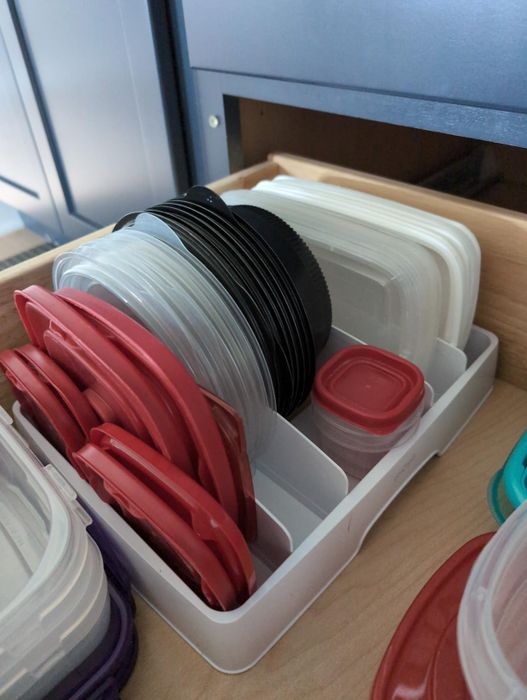 A neatly arranged drawer filled with various plastic container lids stored in a holder for easy access.