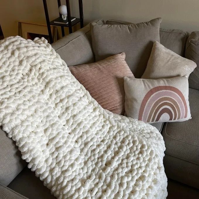 A cozy nook in the living room featuring a soft, textured white knit throw draped over a sofa, accompanied by decorative pillows, including a minimalist rainbow-patterned design.