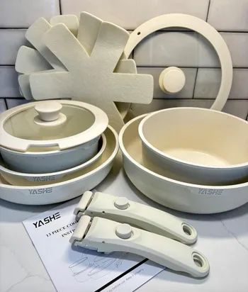 YASHE 13-piece cookware set, featuring non-stick pots, pans, interchangeable handles, lids, and felt protectors. Its neutral color makes it a versatile choice for any kitchen.