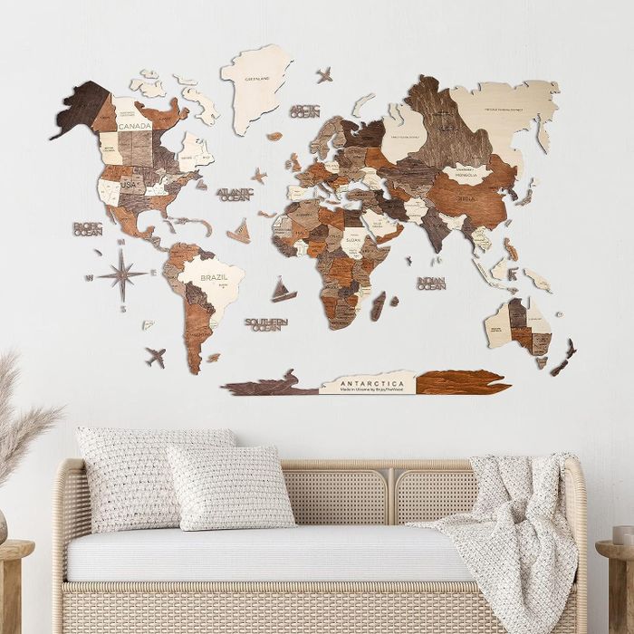 Wooden world map wall decor displayed above a wicker bench adorned with cushions in a modern living room.