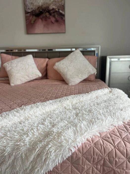 A bedroom featuring a perfectly arranged bed with decorative cushions and a cozy throw blanket draped at the foot of the bed
