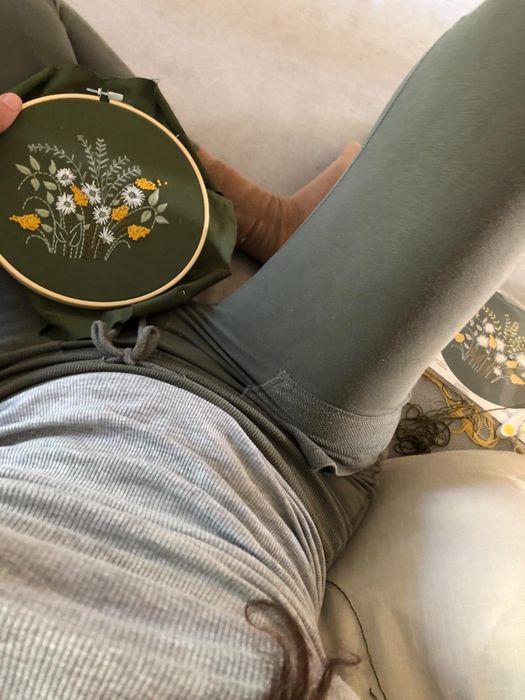 A person seated in casual attire, stitching floral designs into fabric inside an embroidery hoop.