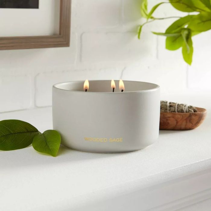 A three-wick candle in a ceramic jar sitting on a shelf, filling the room with its soothing fragrance