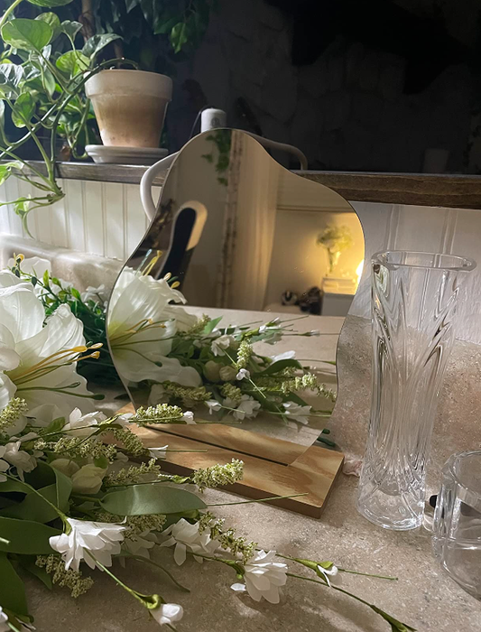 A reviewer shows off the quirky, upright mirror on a table adorned with flowers