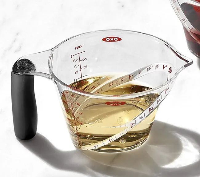 The clear, angled measuring cup filled with oil.