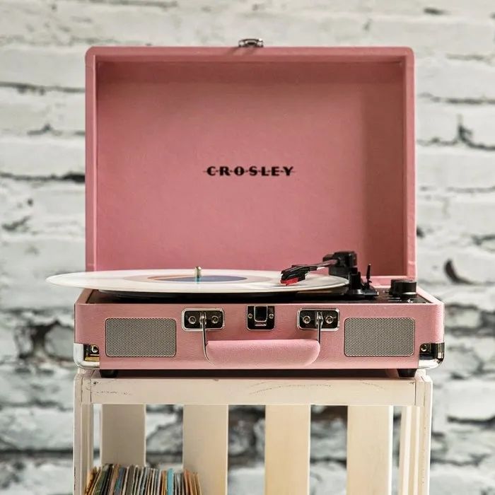 An open Crosley record player with a vinyl on the turntable, placed on a sleek white stand against an exposed brick wall—perfect retro decor vibes.