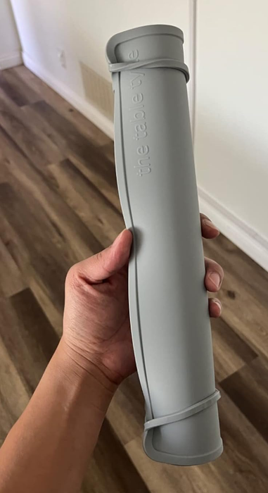 A hand holding a grey Dagne Dover yoga mat carrier against an indoor background.