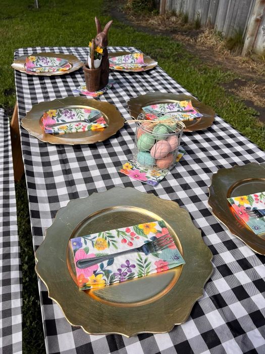 An outdoor table setting with patterned plates, napkins, and a centerpiece, all arranged on a checkered tablecloth for a shopping article.