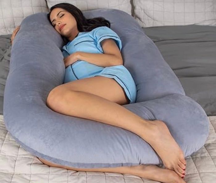 A person sleeping soundly on a large, supportive body pillow, dressed in comfortable sleepwear.