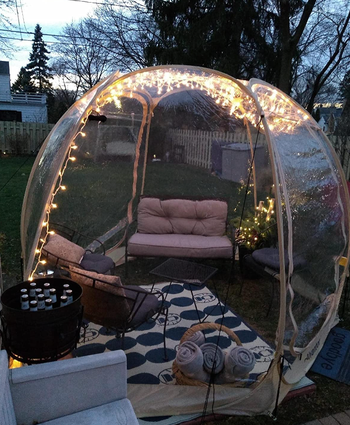 A reviewer's tent set up on their back porch, furnished with comfy furniture and adorned with string lights.