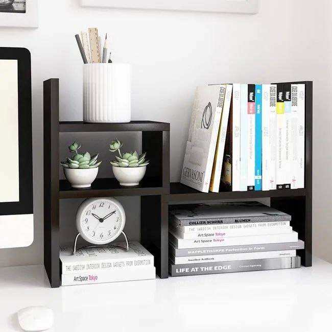 A black shelf featuring two levels of books on the right, with small plants, a clock, and other decorative items arranged on the left side.