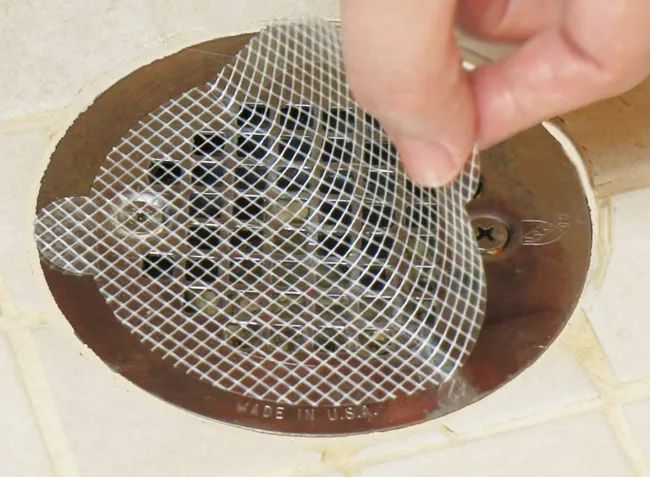 A small, clear circular sticker being applied to a flat shower drain