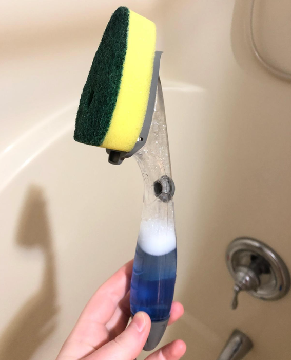 Reviewer holding a sponge attached to a handle filled with soap, ready for effortless dishwashing.