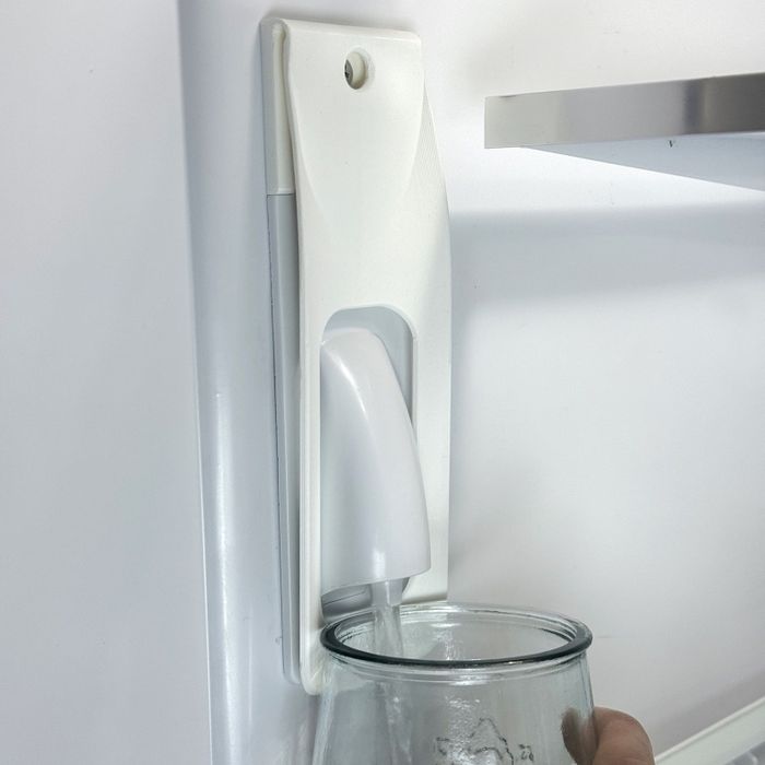 A person filling a glass with water from a refrigerator’s dispenser.