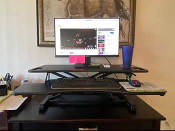 The same desk riser now holds a monitor on a black desk, providing a sleek setup.