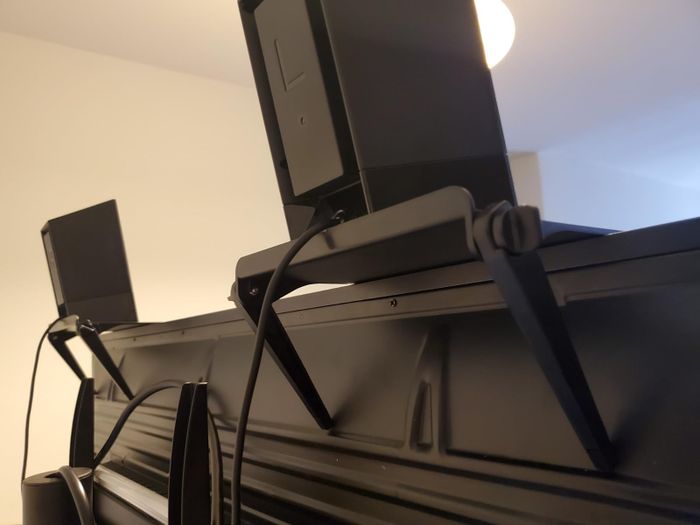 A reviewer photo of the shelf attached to a TV screen, holding a small speaker.
