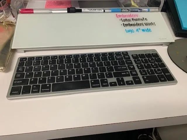 A reviewer's photo showing the long rectangular whiteboard with a groove at the top holding markers, and a keyboard placed in front.