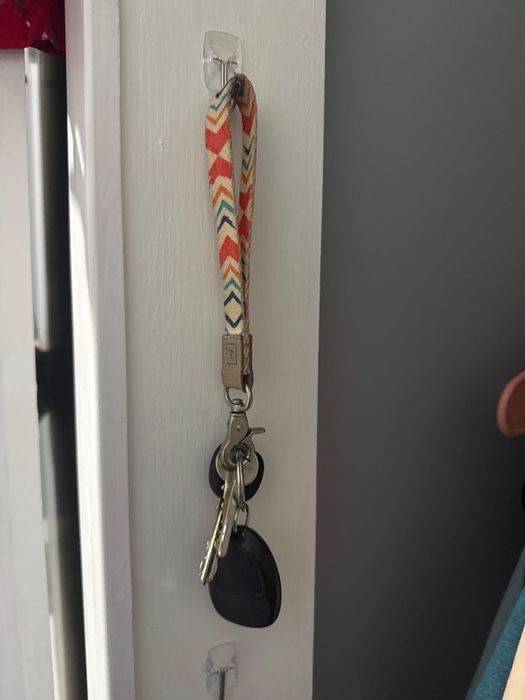 A keychain with a chevron-patterned strap hanging from a wall hook, holding a set of keys and a car remote.