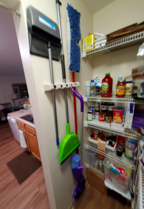 A small kitchen pantry featuring a row of hooks with brooms and mops neatly hung up and stored out of sight.