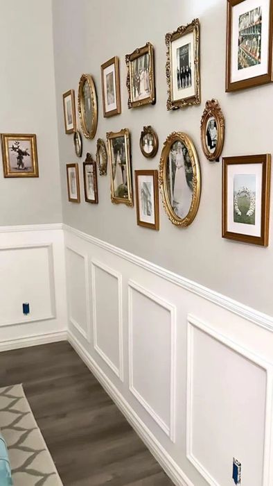A gallery wall showcasing a variety of framed pictures above a white-wainscoted wall with hardwood floors