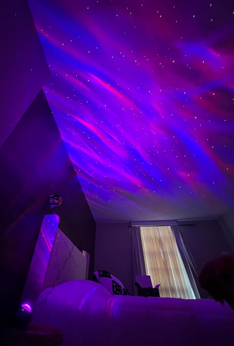 A reviewer’s photo showing the projector casting pink and purple light across their bedroom ceiling.