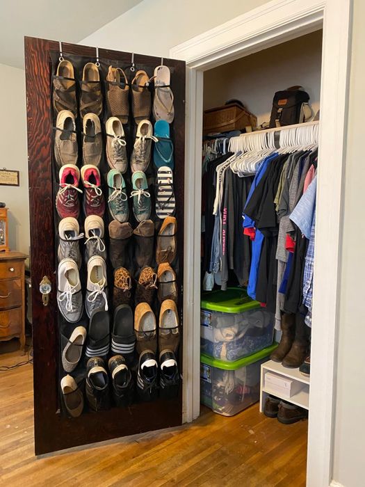 A closet featuring an over-the-door shoe organizer filled with various shoes, beside hanging clothes and storage bins.