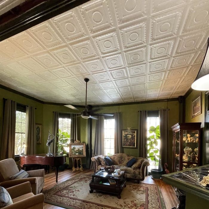 A retro-inspired living room featuring intricate ceiling tiles, antique furniture, and a cozy, patterned rug
