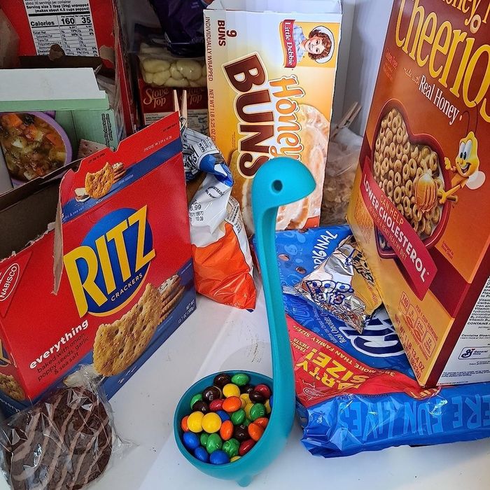 A packed pantry shelf overflowing with snacks, cereals, and a charming blue dinosaur-shaped container brimming with colorful candies.