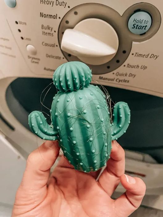 A reviewer holding a silicone cactus dryer ball with a significant amount of hair caught on it.