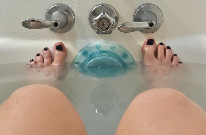 Feet soaking in the tub, next to the drain cover