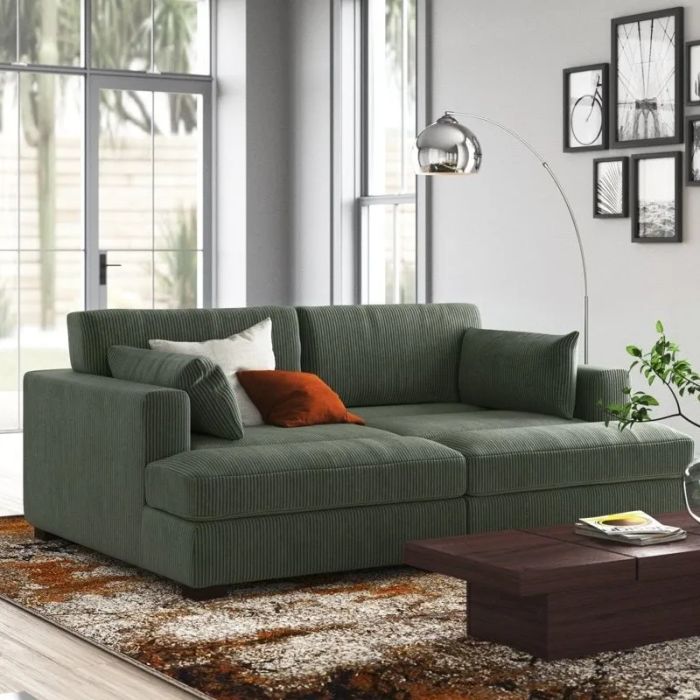 A chic green corduroy sofa adorned with plush cushions in a contemporary living room, complemented by a stylish floor lamp, modern wall art, and a sleek wooden coffee table.