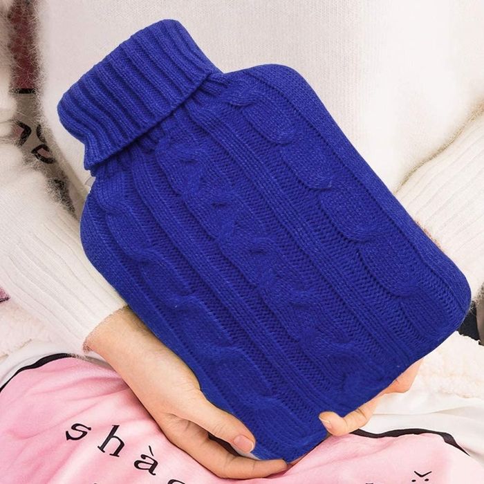 A model holding the hot water bottle, cozy in its blue knit cover
