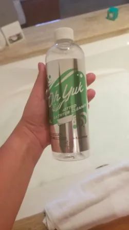 A reviewer's hand holding the bottle of jetted tub cleaner.