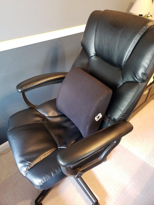 An ergonomic black office chair with a lumbar support cushion placed on the seat for added comfort and support.